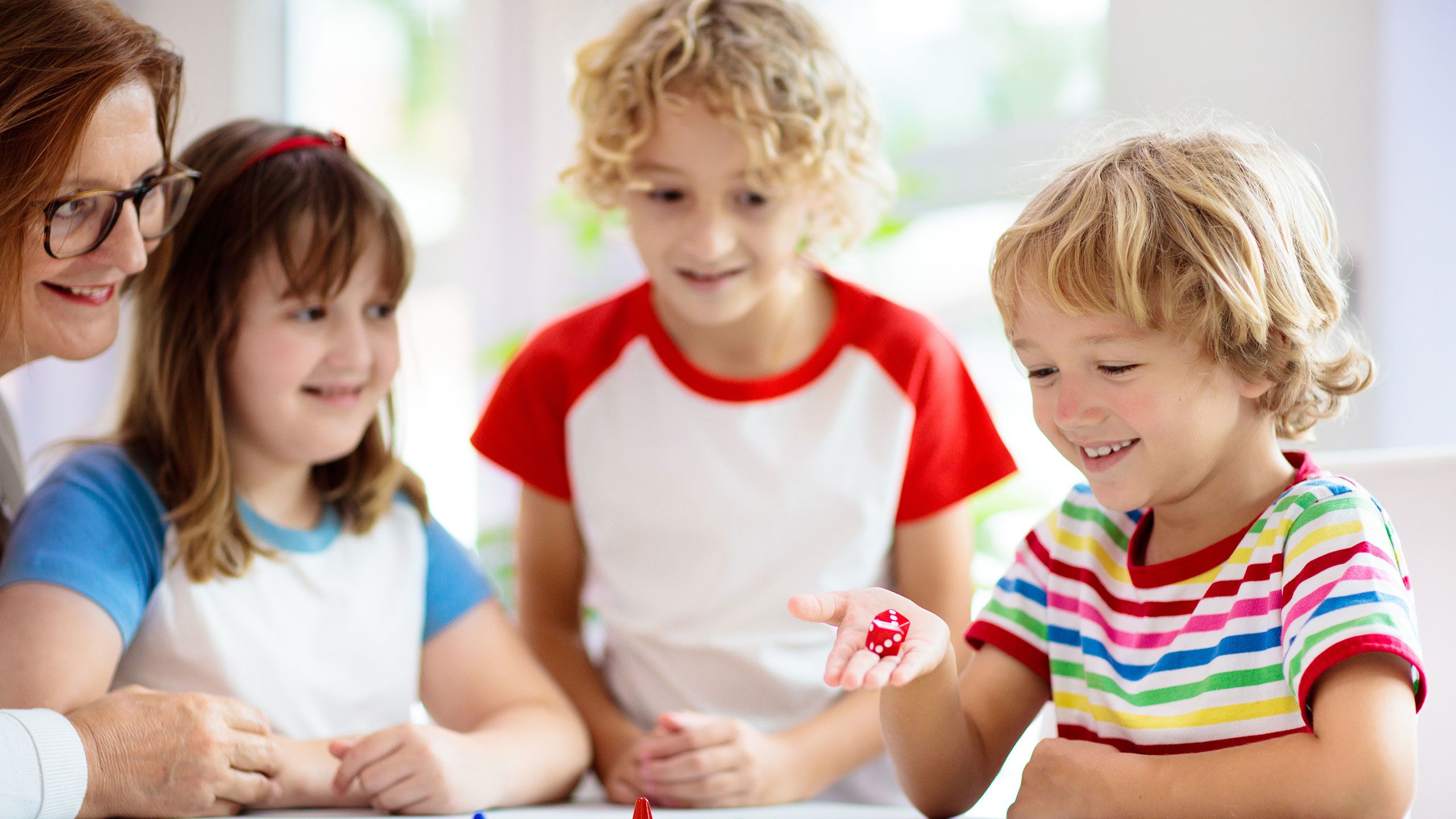 A young child rolls dice while playing a game with family.