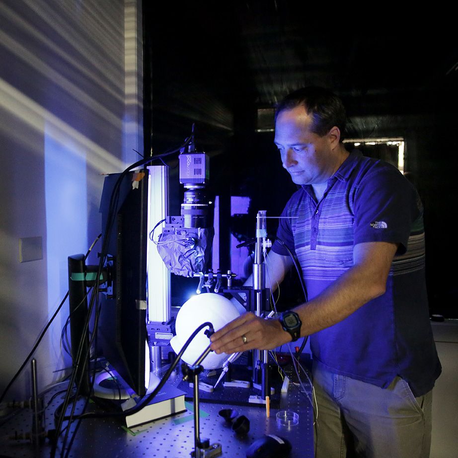 Cris Niell stands at a lab bench illuminated with a purple light, holding equipment
