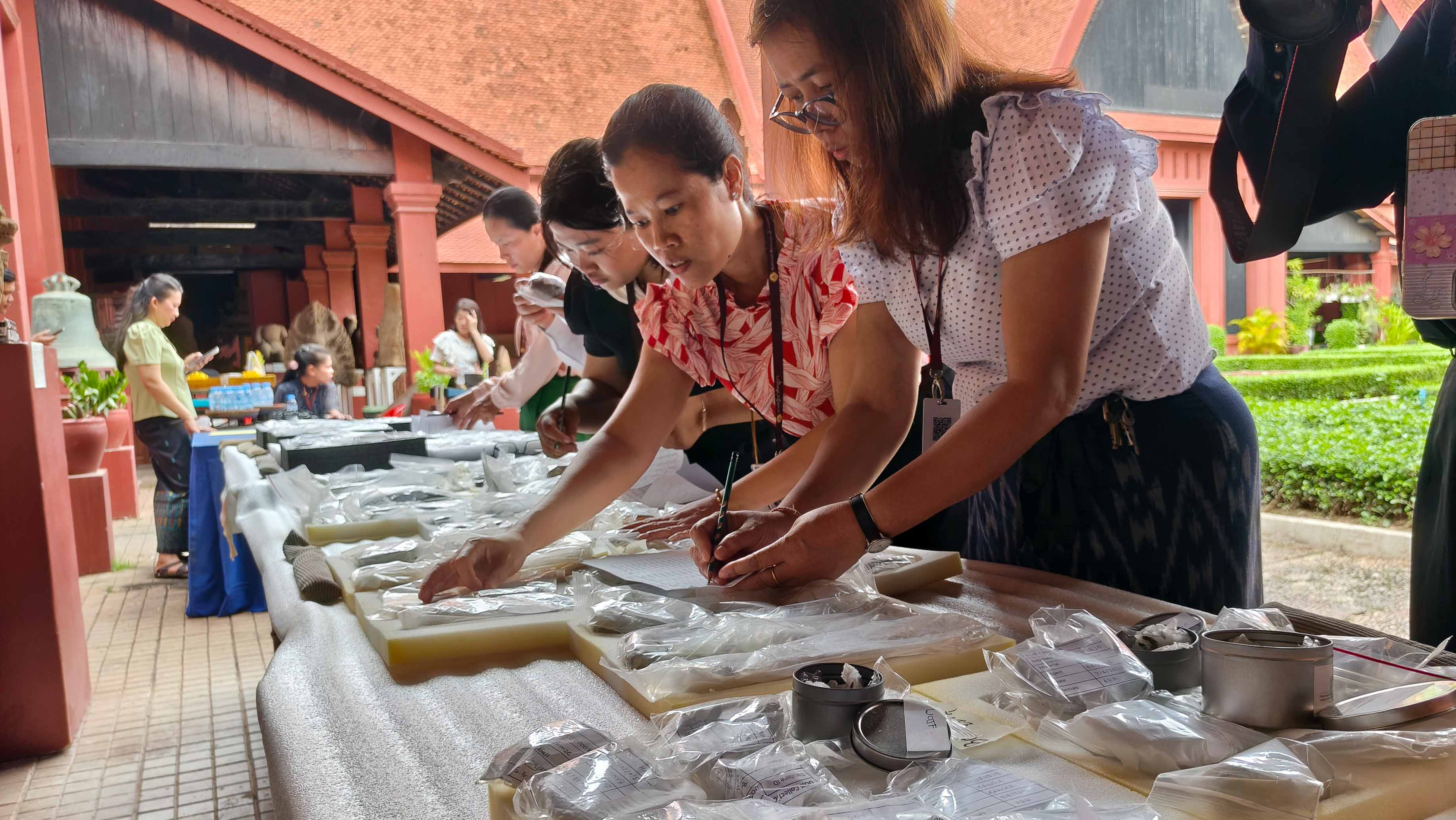 a group of people stand beside a table, sorting through materials