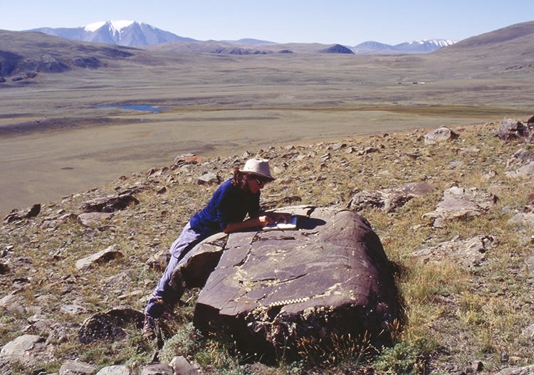 A woman examines a table-like rock in an open, mountainous area
