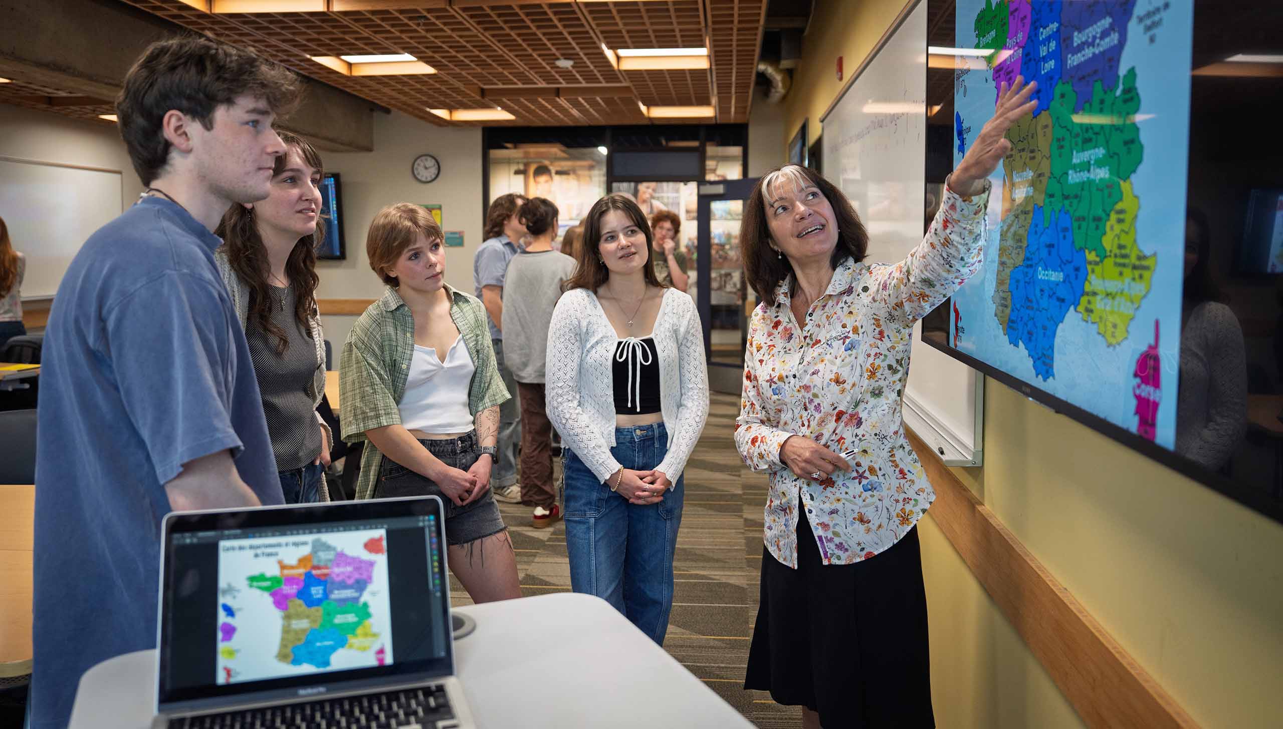 Students gathered around a teacher in front of a map on a big screen