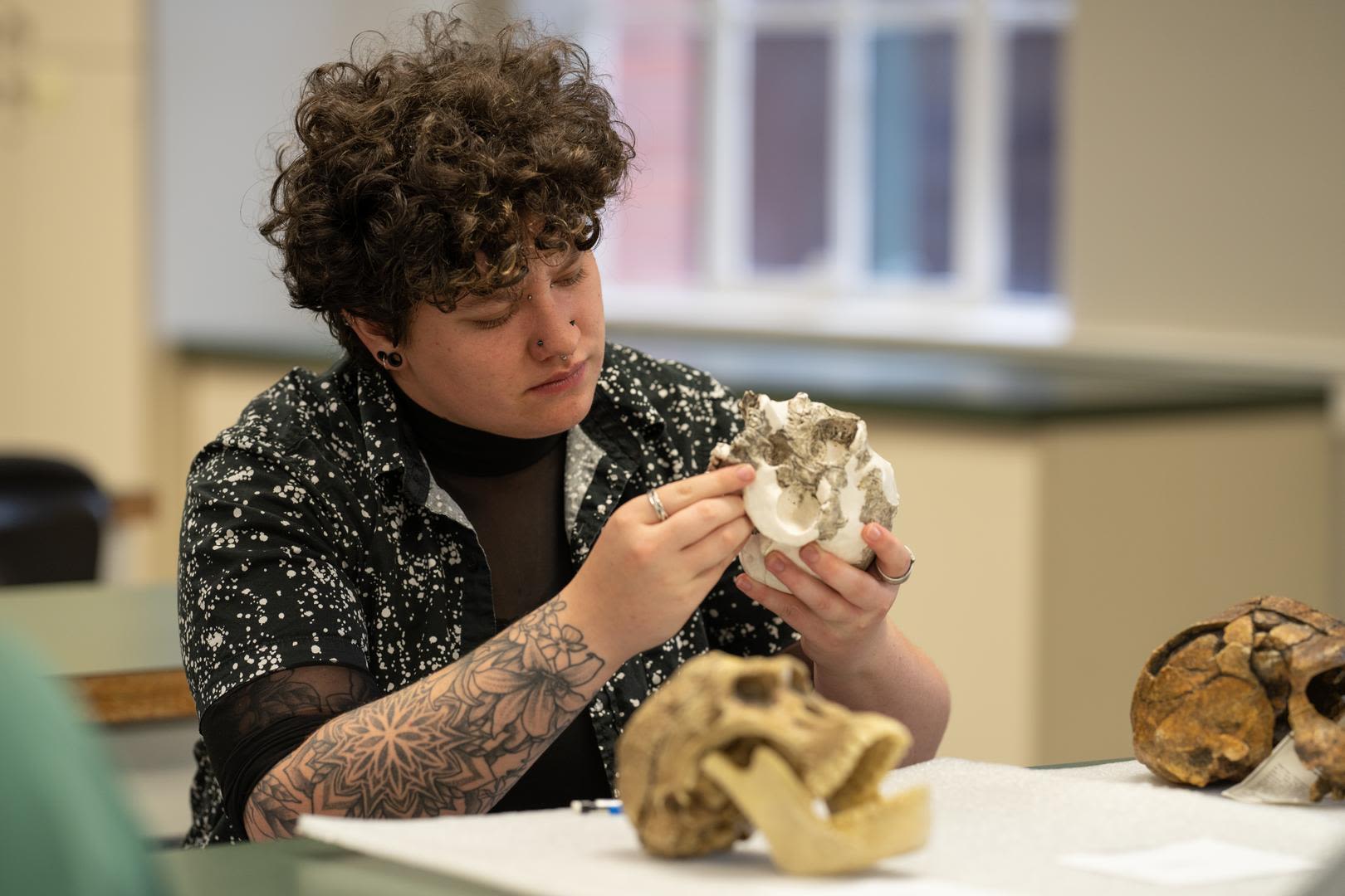student in a classroom examining a skull