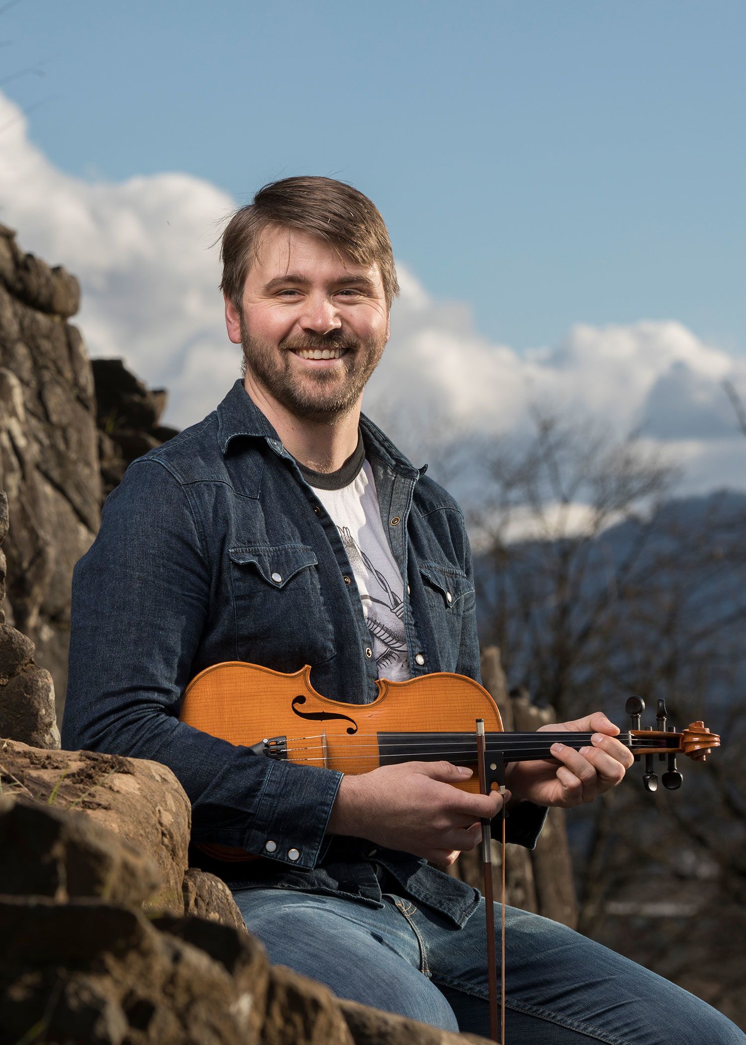 Leif Karlstrom sits atop a rocky mountain with a violin in his hands
