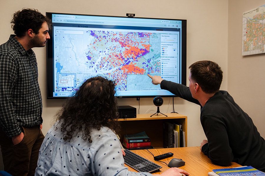 Three people look at a map on a large screen
