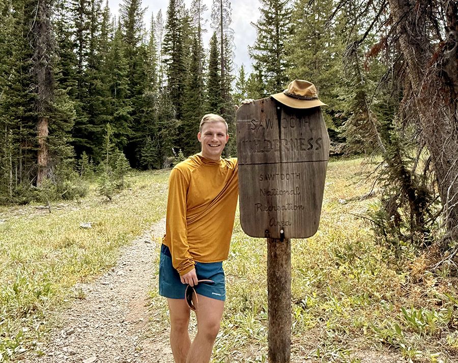 Person stands next to sign on hiking trail in a forest