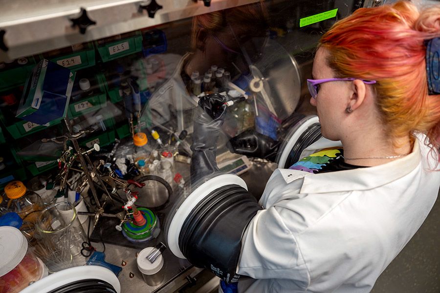 Student in lab coat and glasses with hands in gloves that go through holes