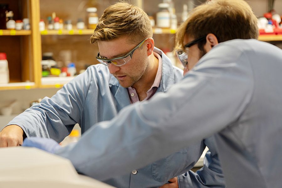 Two people in safety glasses and lab coats looking at instrument