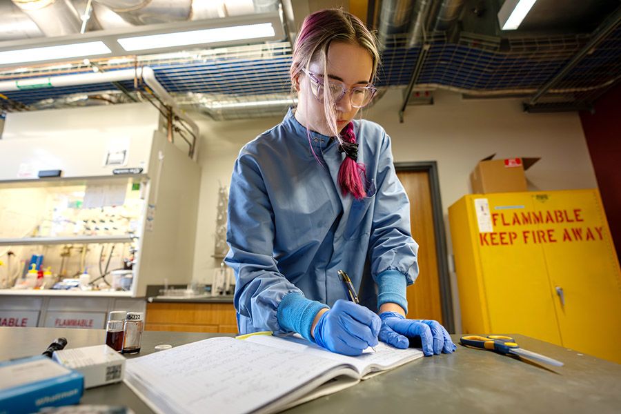 Person in lab coat writing in a notebook